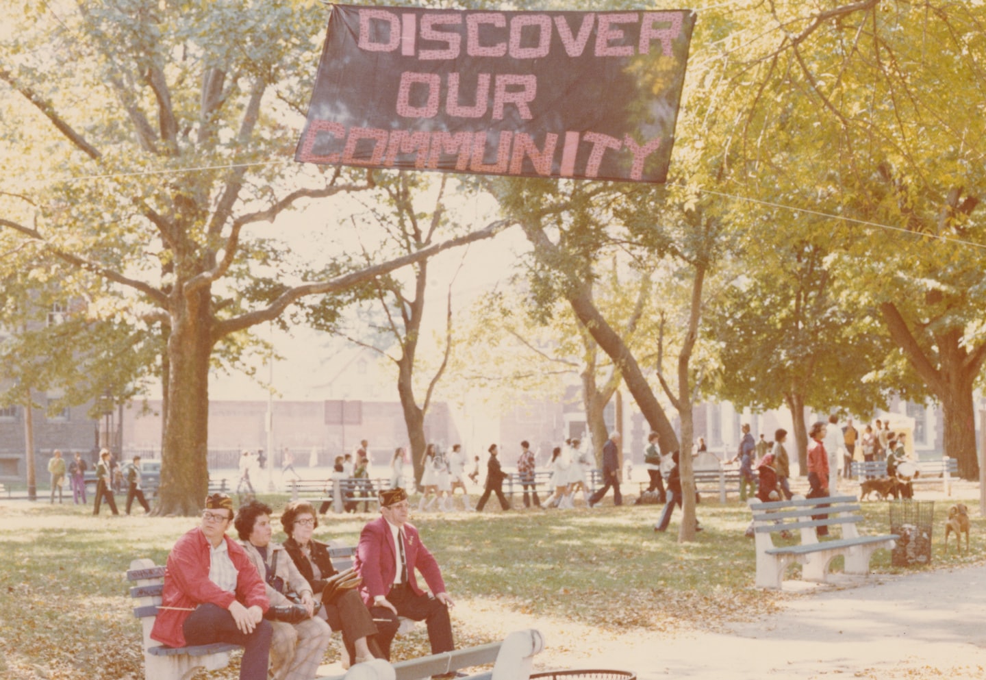 Veterans sit on a park bench watching a community gathering.