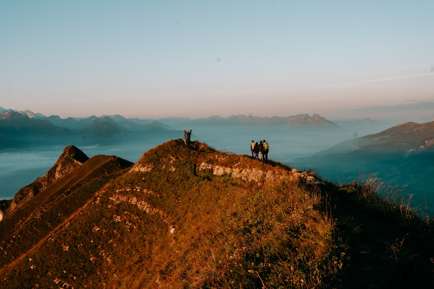 Five hikers standing on a grassy mountain ridge overlooking a valley.